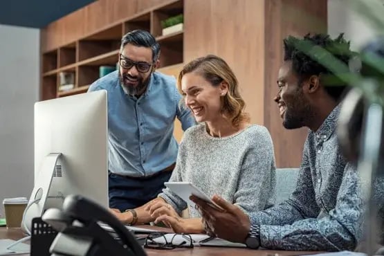 Équipe professionnelle souriante travaillant ensemble devant un ordinateur pour traiter les problèmes d’impayés