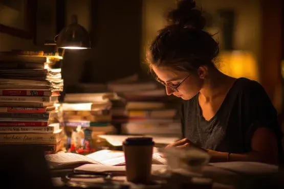 Une jeune femme rédige un mail dans une ambiance nocturne, entourée de livres