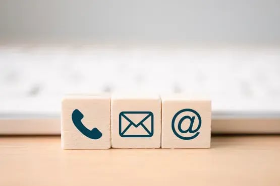 Blocs en bois affichant les icônes téléphone, email et arobase devant un clavier