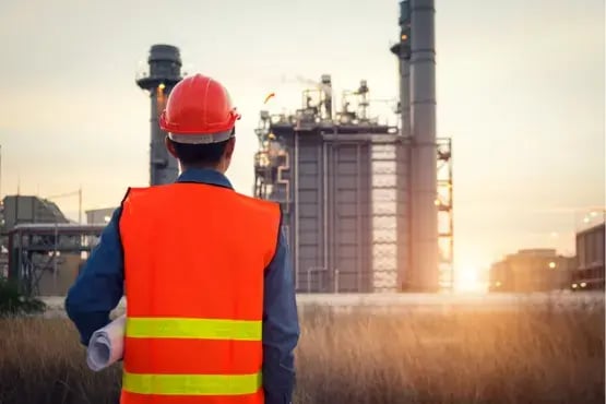 Technicien en gilet fluorescent observant une installation industrielle au coucher du soleil
