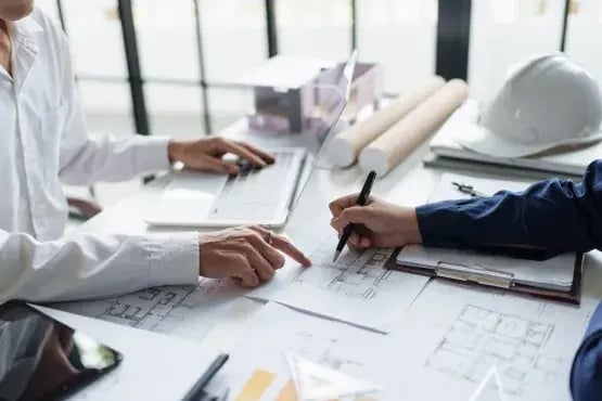 Deux personnes en réunion examinant des plans d’architecture avec un ordinateur