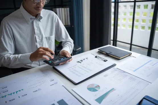 Consultant utilisant une calculatrice avec des documents financiers étalés sur un bureau