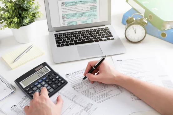 Main calculant des honoraires d’architecte à l’aide d’une calculatrice et de documents fiscaux