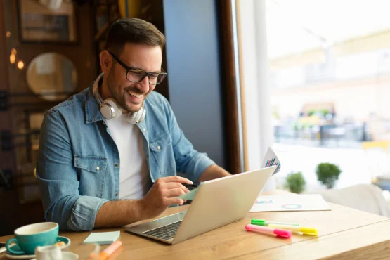 Un freelance souriant travaille sur son ordinateur portable dans un café avec des graphiques devant lui